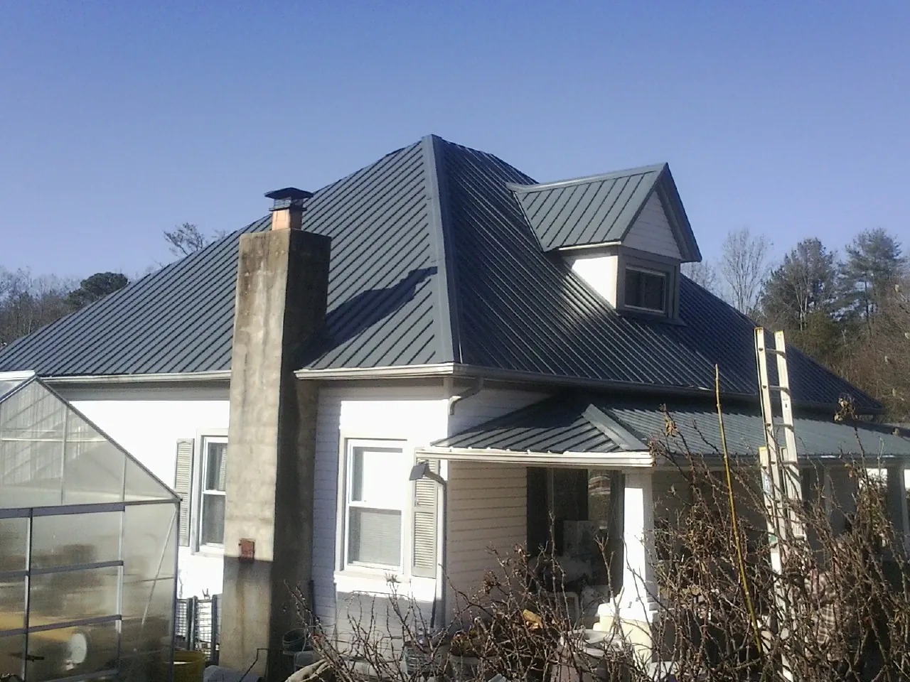 Dark blue standing seam metal roof on a white farmhouse with dormer — Slate & Tile Roof Repair by Roofing Brothers in Gilbertville