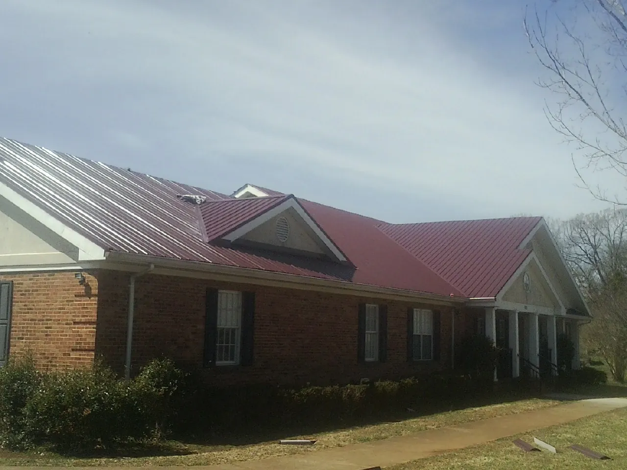Red metal roof with gabled entries on a long brick building, from a Hail Damage Roof Repair job in Gilbertville