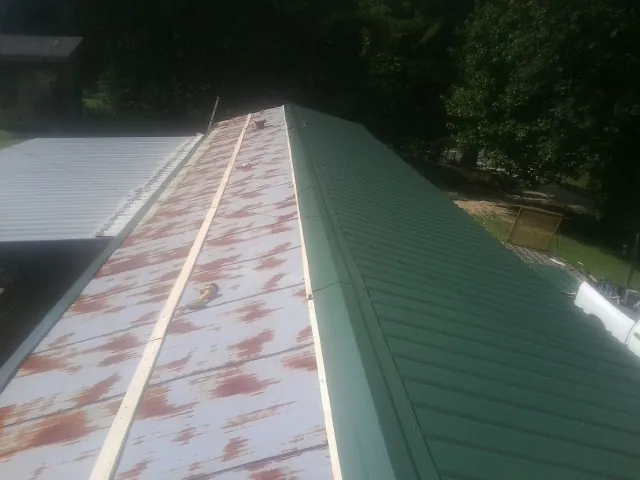 Old rusted panels beside newly installed green metal roofing — Wind Damage Roof Repair by Roofing Brothers in Gilbertville