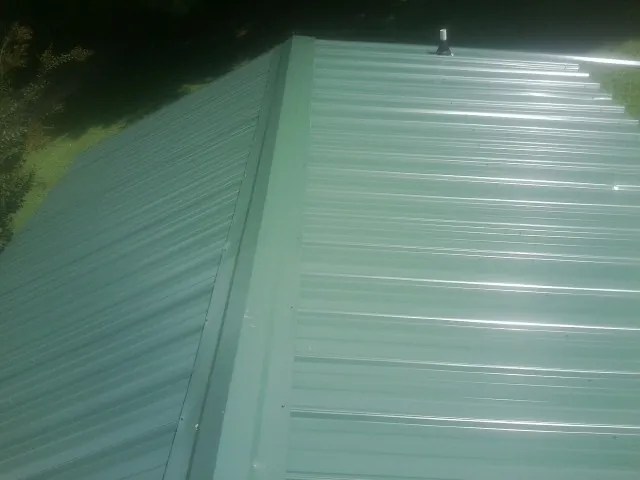 New green metal panels meeting at the ridge of a roof — Flat Roof Repair work by our crew in Gilbertville