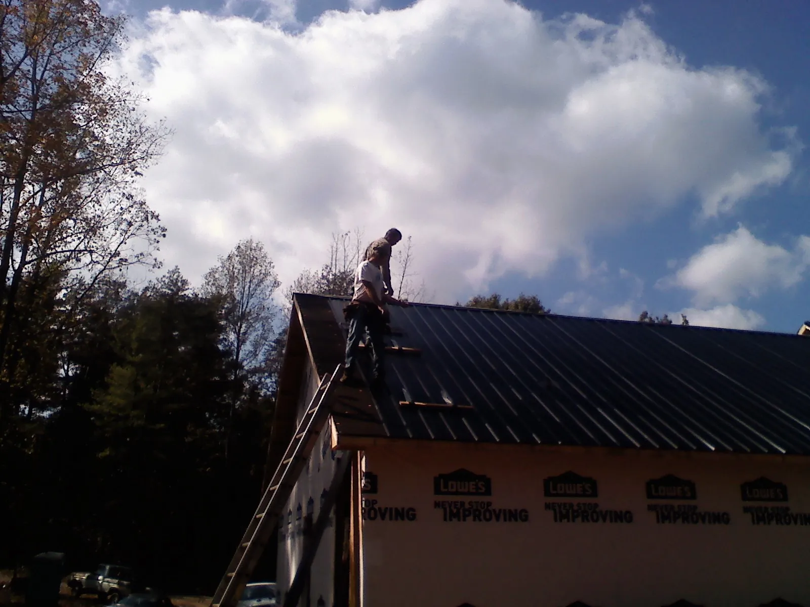 Roofer fastening dark metal panels high against a cloudy sky, from a Roof Inspection job in Gilbertville