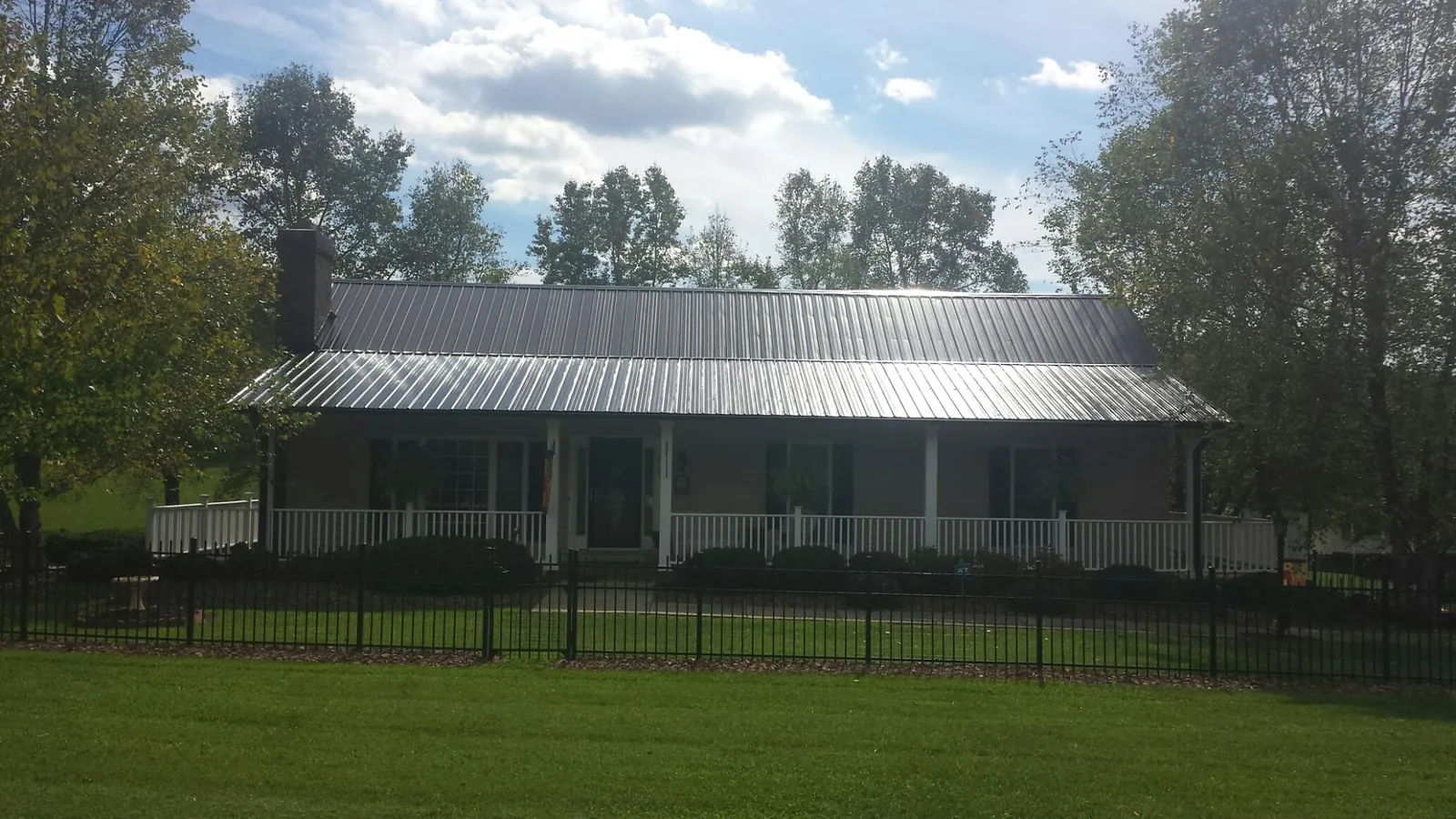 Gray metal roof on a brick ranch with a full width front porch — Gutter Guard Installation work by our crew in Gilbertville