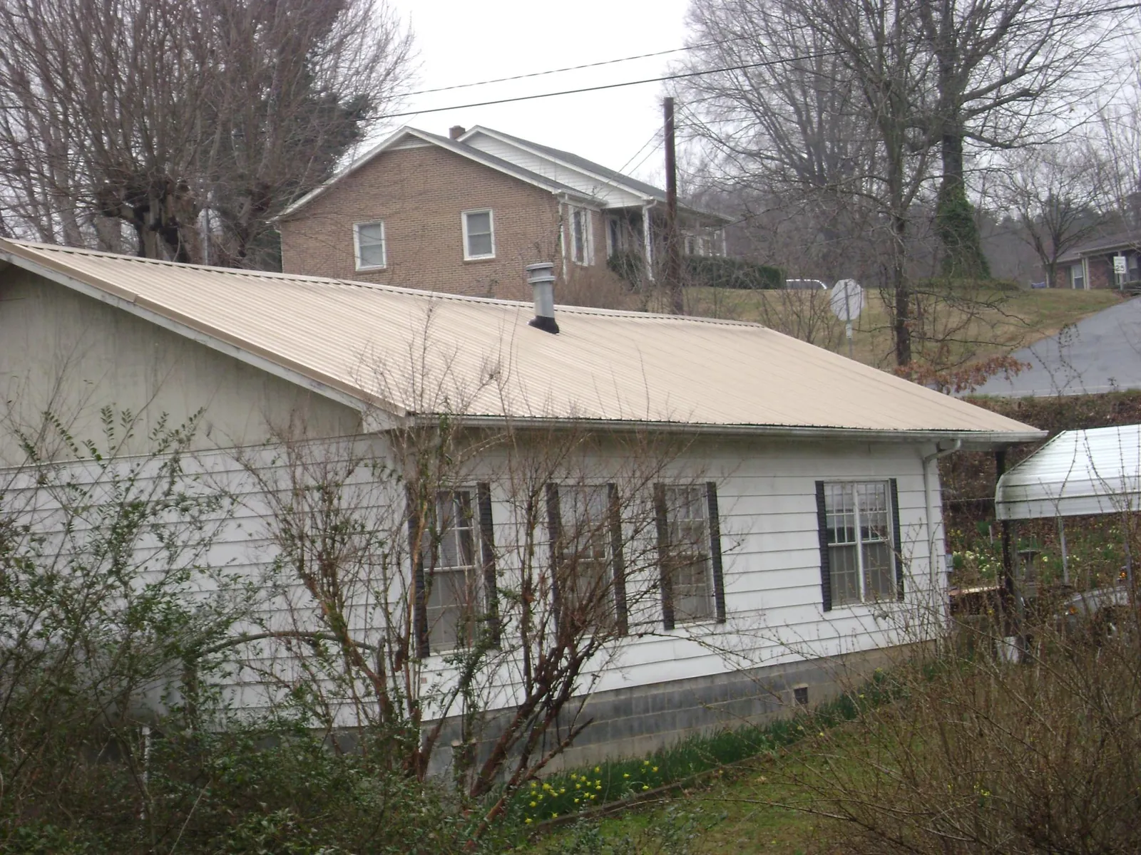 Tan metal roof on a white sided house set into a hillside — Commercial Roofing by Roofing Brothers in Gilbertville