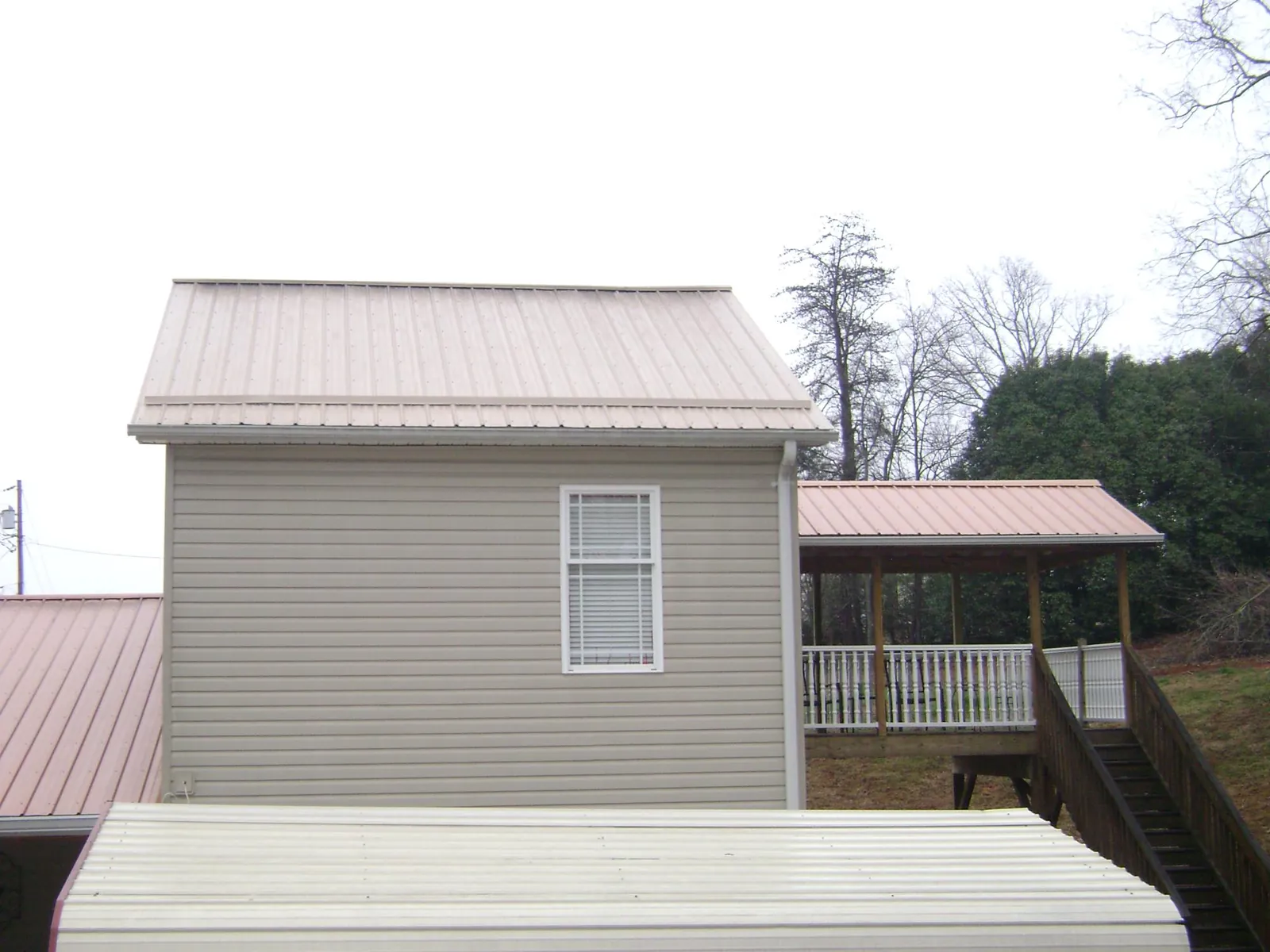 Tan metal roofs on a two story addition and attached porch, from a Roof Replacement job in Gilbertville