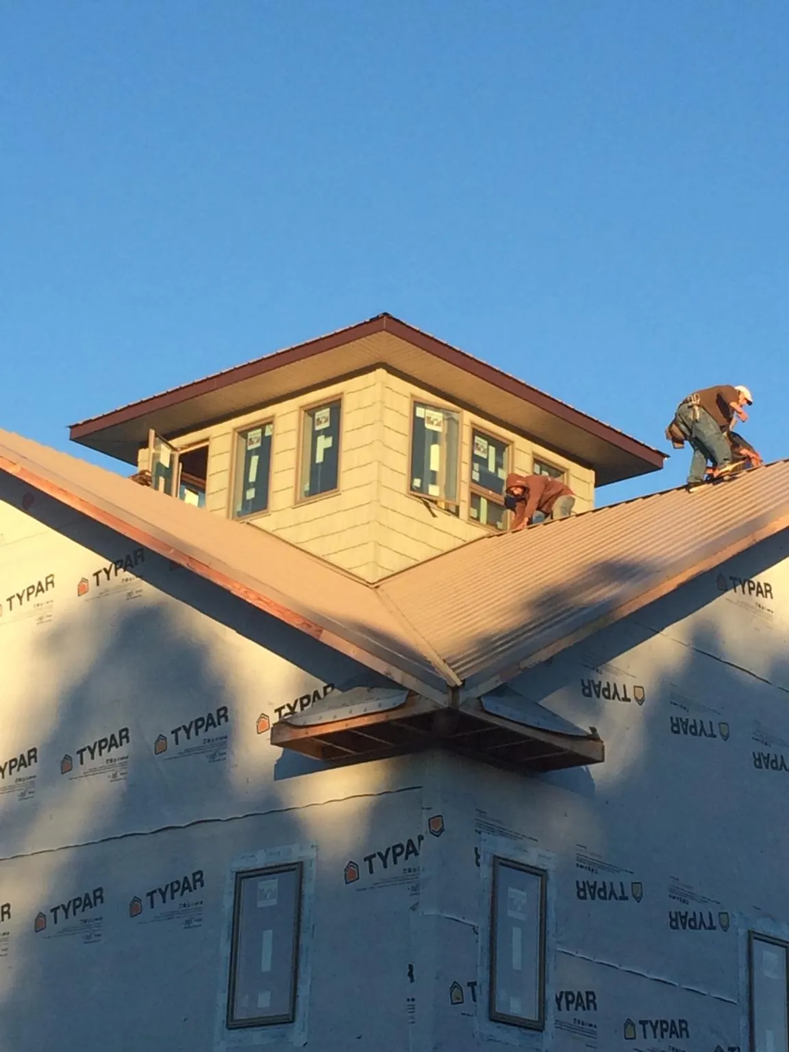 Roofers working around a rooftop cupola on a new metal roof at sunset — Roof Waterproofing in Gilbertville by Roofing Brothers